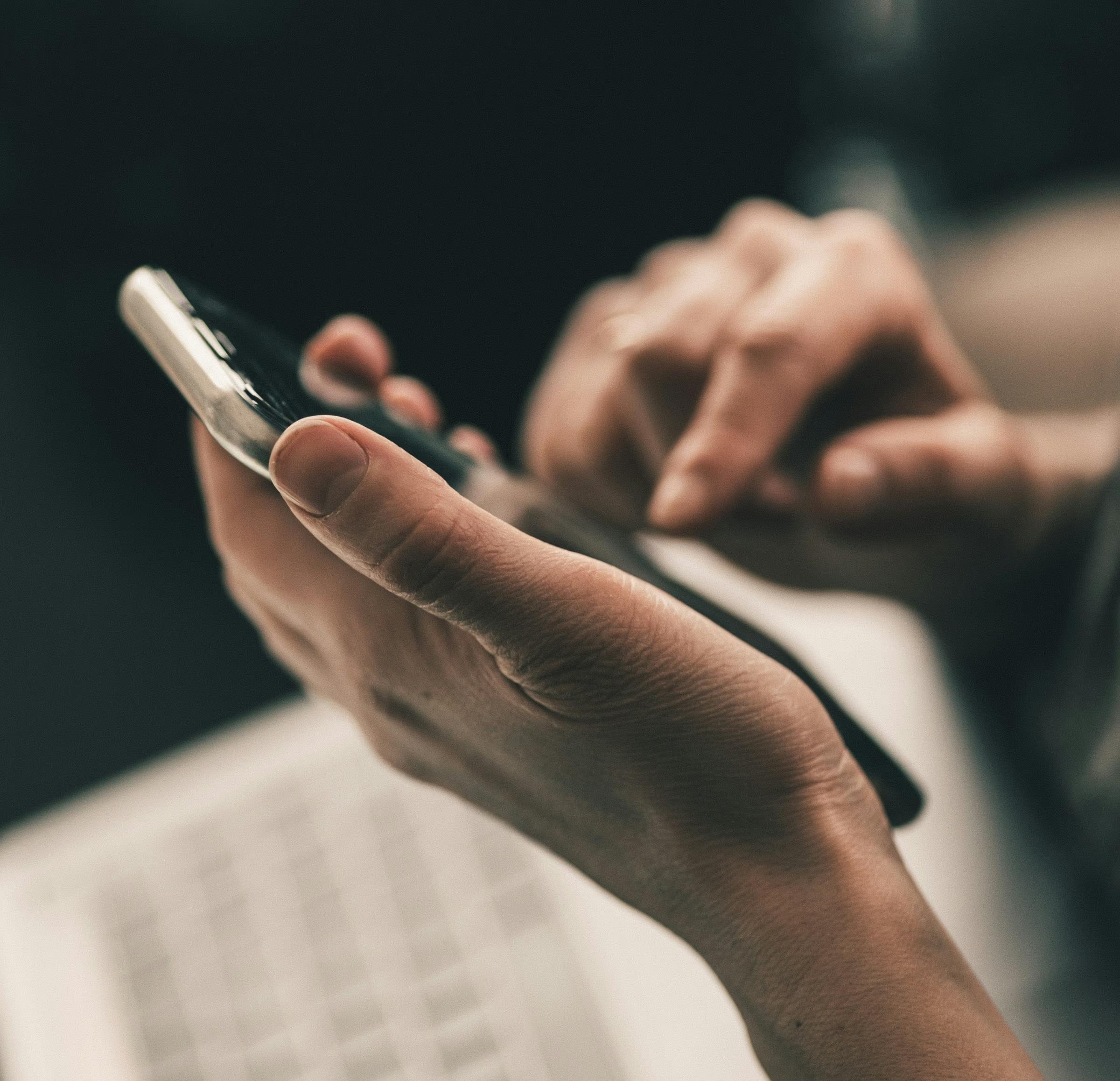 Dizüstü bilgisayarın başında, elindeki telefonla arama yapan bir kişi