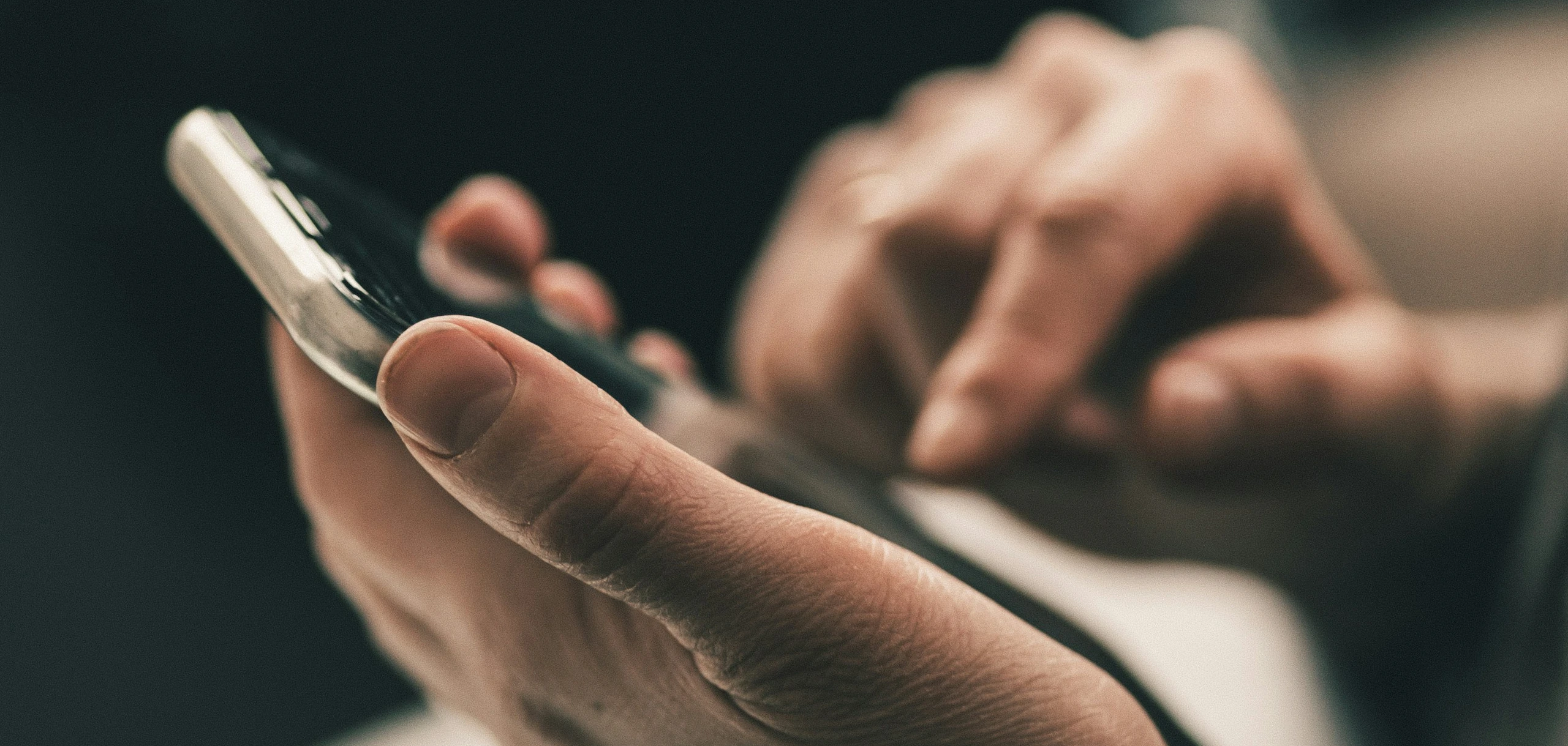 Dizüstü bilgisayarın başında, elindeki telefonla numara çeviren bir kişi; yakın plan.